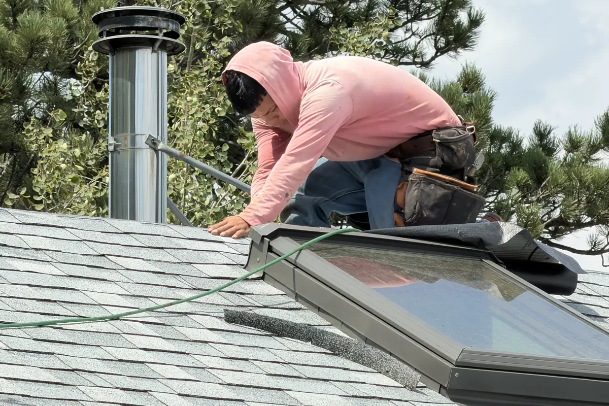 Roofer setting new flashing at a skylight next to a stainless chimney pipe
