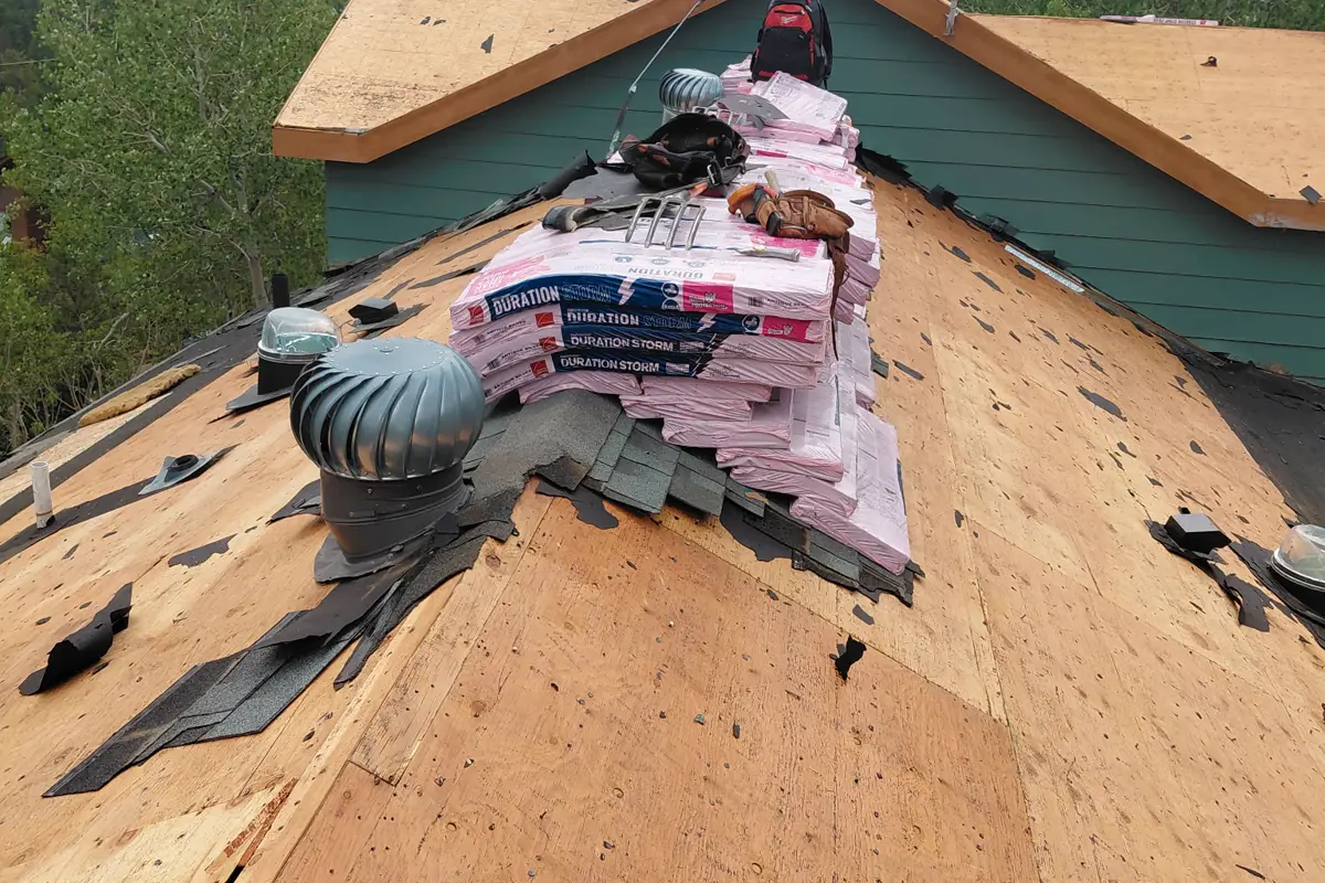 Roof torn off to bare sheathing with new shingle bundles staged along the ridge